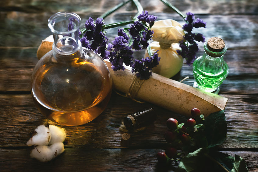 Herbal medicine essential oil and various herbs on a table and ancient recipe scroll. Witchcraft.